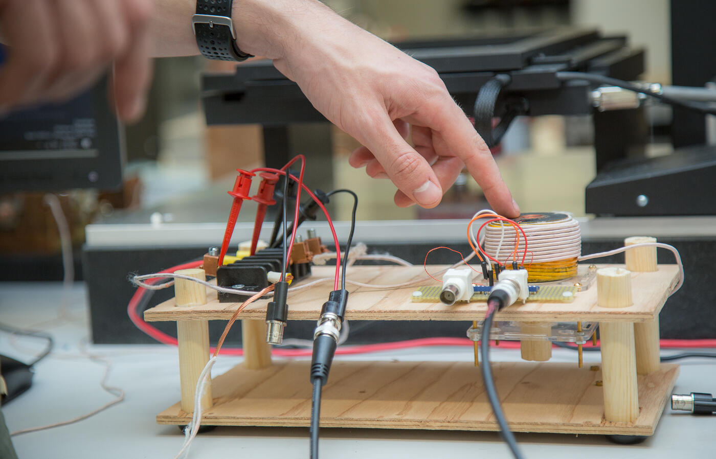 A person points to a device on a wooden circuit board.